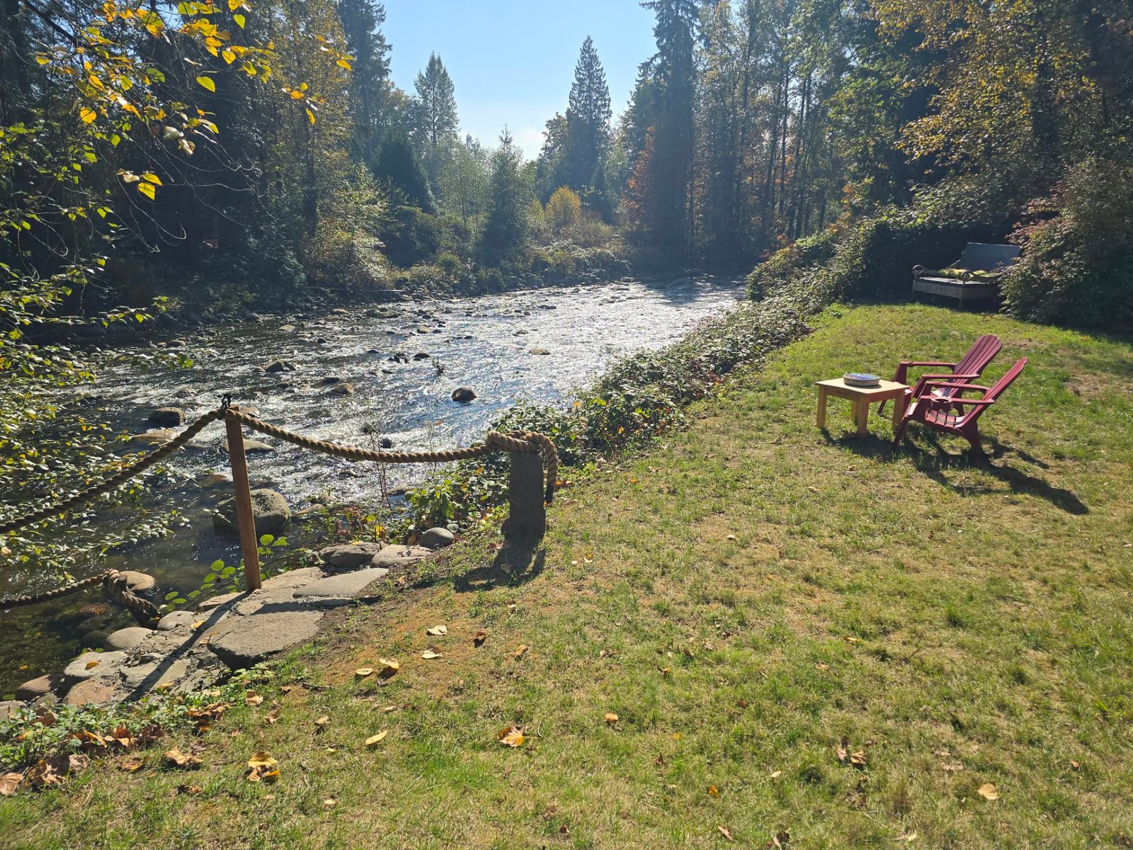 Riverbank lawn with two red Adirondack chairs and rope-railed stone steps down to the Seymour River